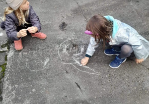 Dzieci rysują kolorowymi kredami na betonie.